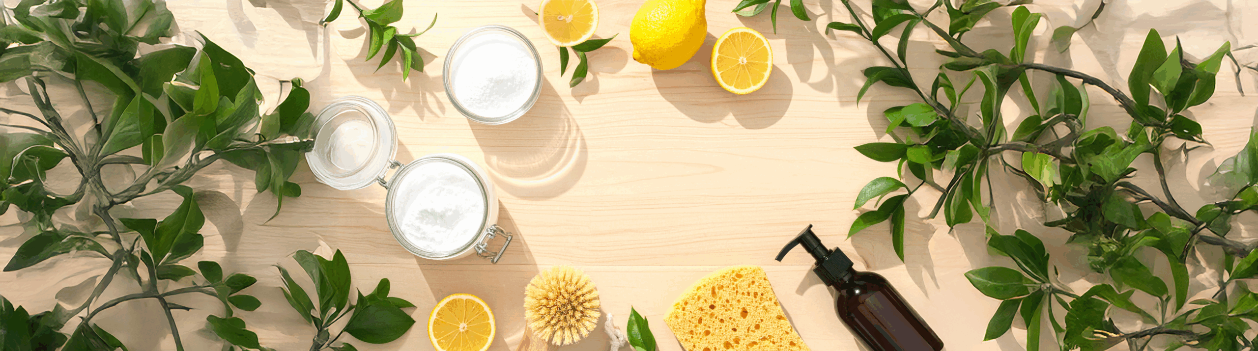 5 Astuces Ménage Écologique. Ingrédients naturels pour produits ménagers faits maison, avec du bicarbonate de soude, des citrons, une brosse, une éponge et un flacon réutilisable disposés sur une table en bois clair.