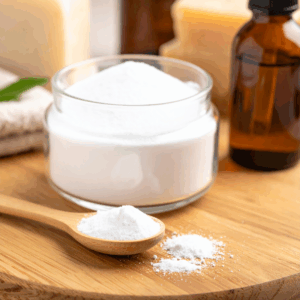 Bicarbonate de soude vrac. Bol en verre rempli de poudre blanche, du bicarbonate de soude, avec une cuillère en bois posée sur une planche en bois clair.